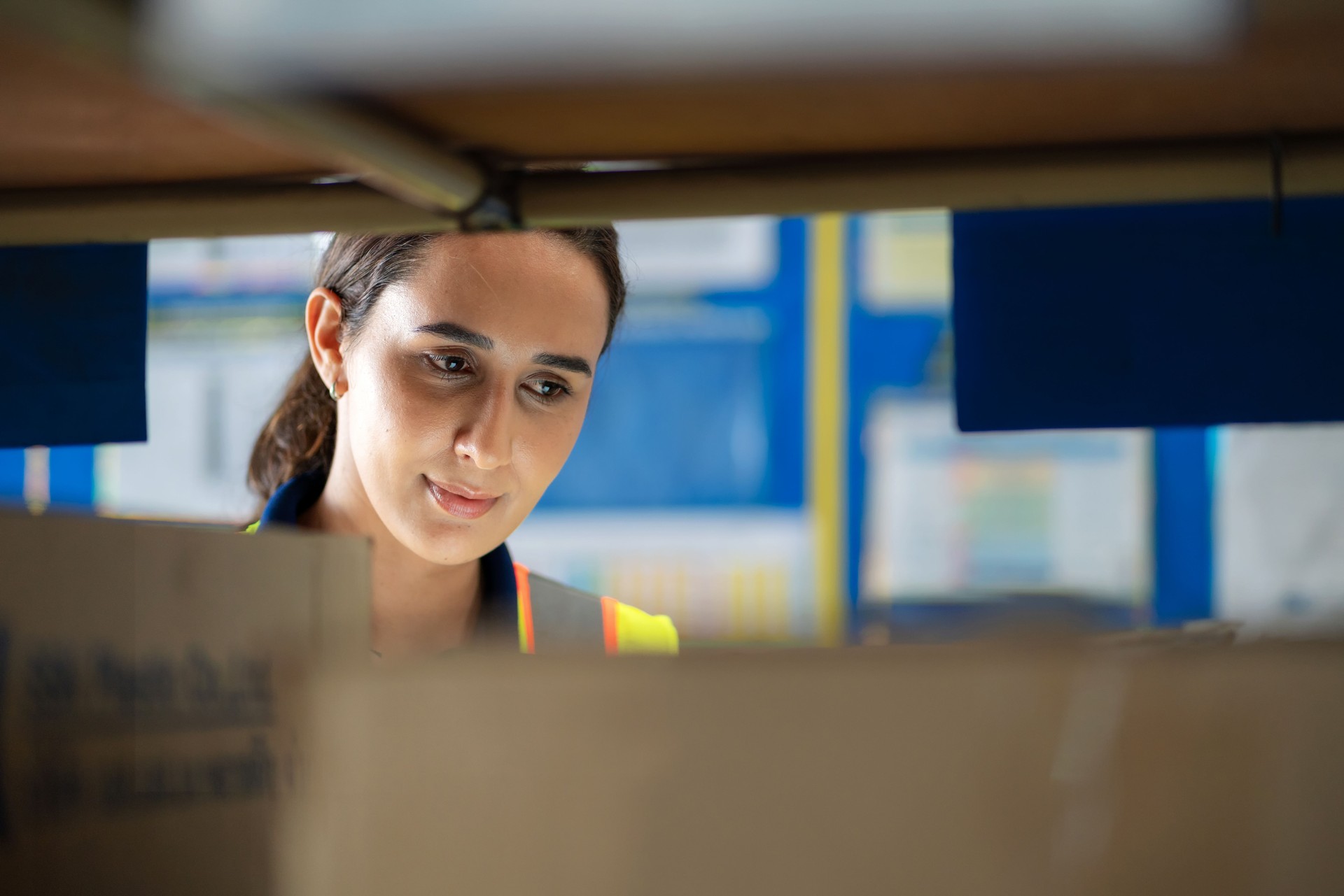 Female warehouse worker in reflective safety gear inspecting inventory on storage shelves. Logistics, supply chain management, and inventory control in a busy distribution warehouse. Industrial efficiency, teamwork, and business strategy in action.